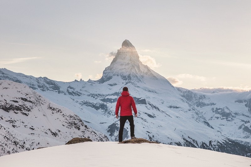 Person standing on edge looking out towards a snowy mountain
