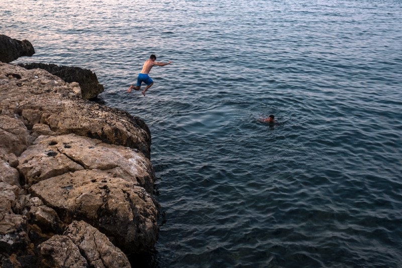 Person jumping into ocean from rocks, swimmer in the water